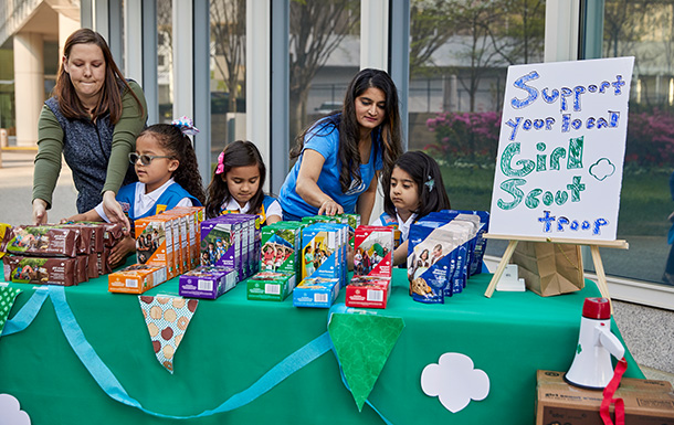 two adult volunteers with a group of girl scout daisies outside selling cookies